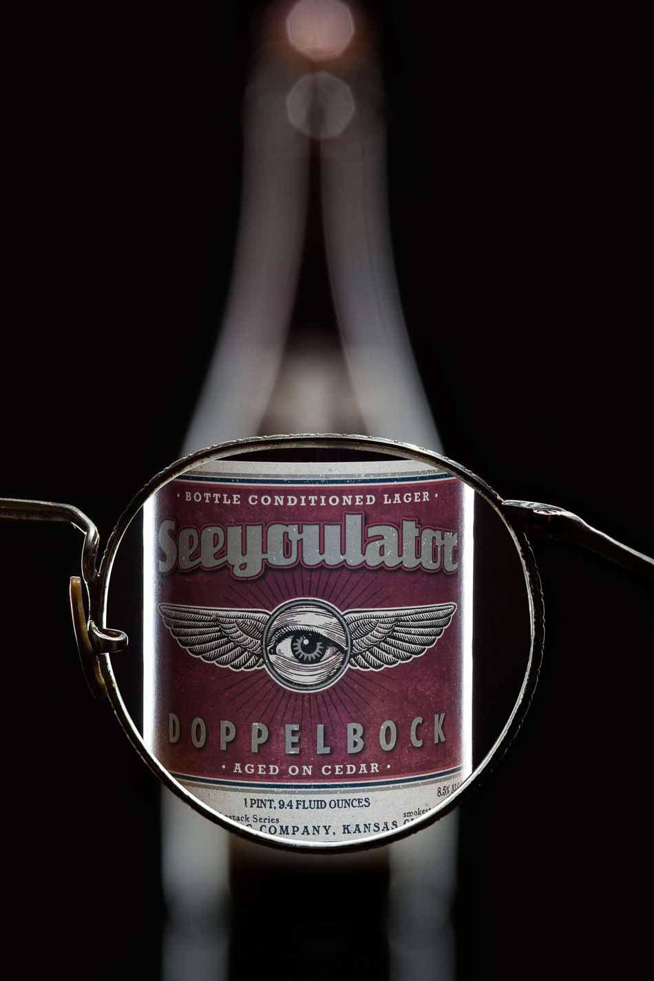 Looking through glasses lens making blurry beer bottle sharp - See You Later Doppelbock Cider | Bottle Photography | Dramatic Product Photography | Still Life Photography | Shot in Denver, Colorado